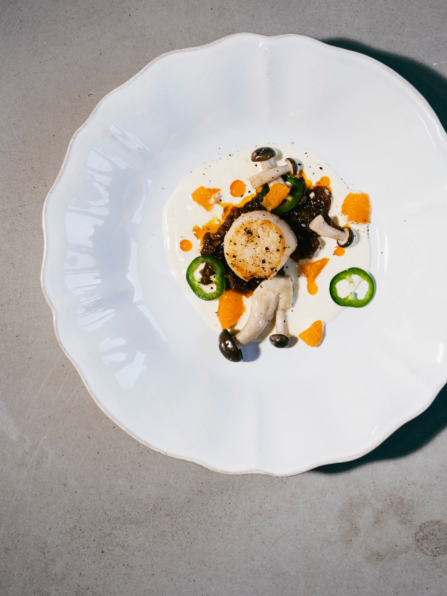 Pilgrimsmussla med svamp, mandarin och jalapeño på vit tallrik